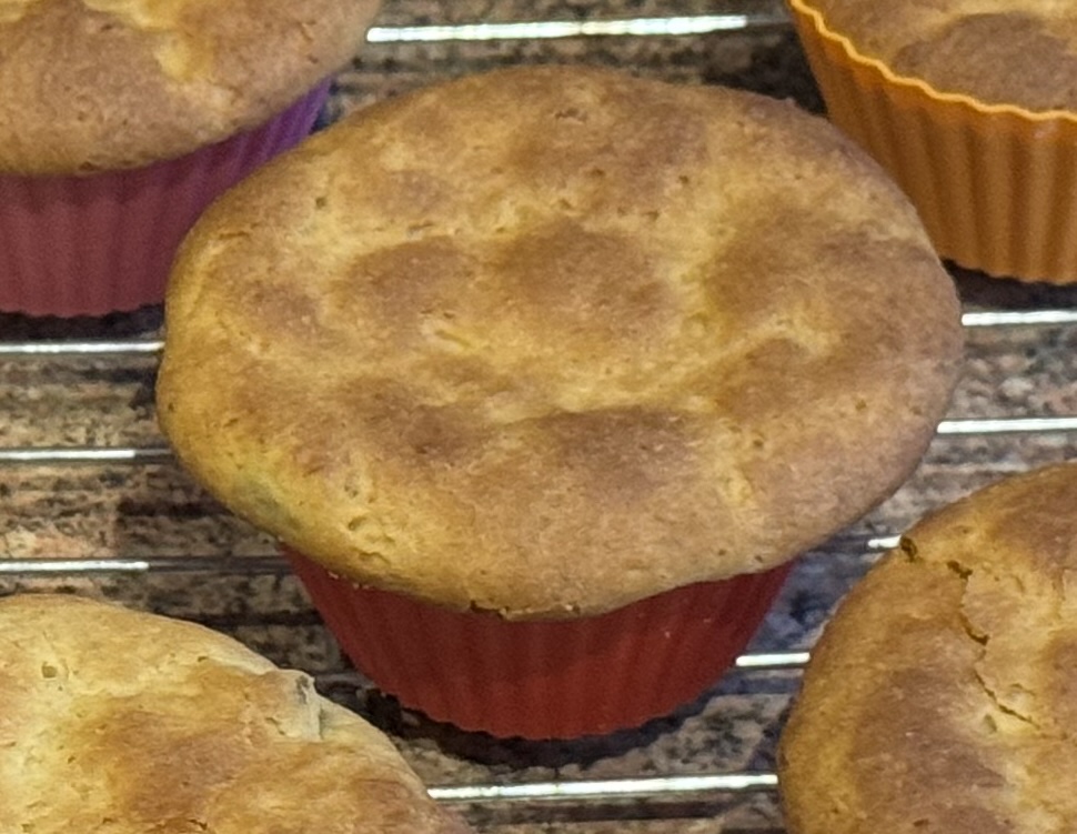 Photograph of a mini-panettone surrounded by its brethren.
The top is golden brown with paler patches.
It has a small amount of muffin top,
going over the sides of the red silicone mould
